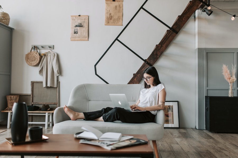 woman sitting on a couch using laptop reading work at home forums