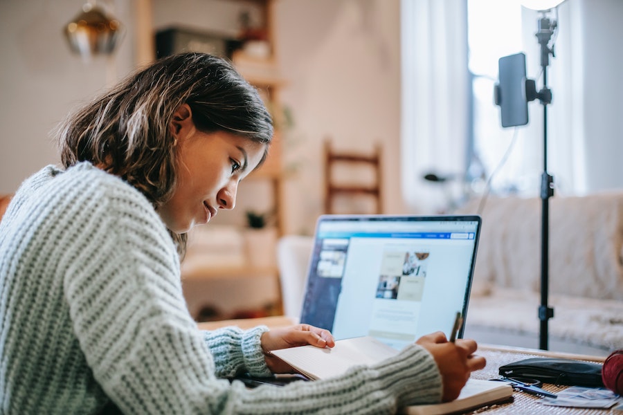 woman writing on notebook in front of laptop