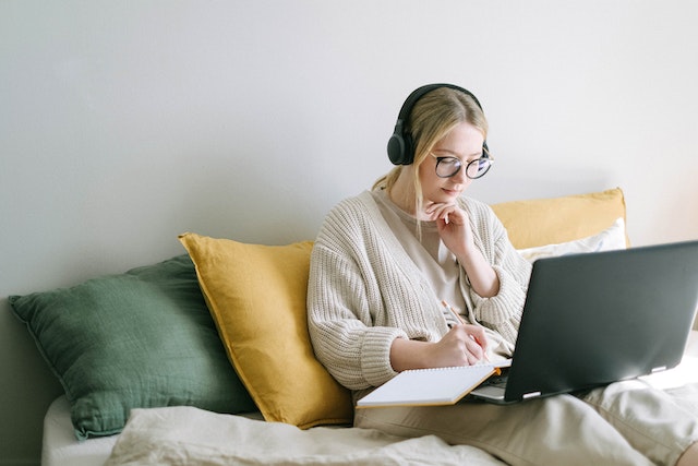 woman on bed writing with laptop in front