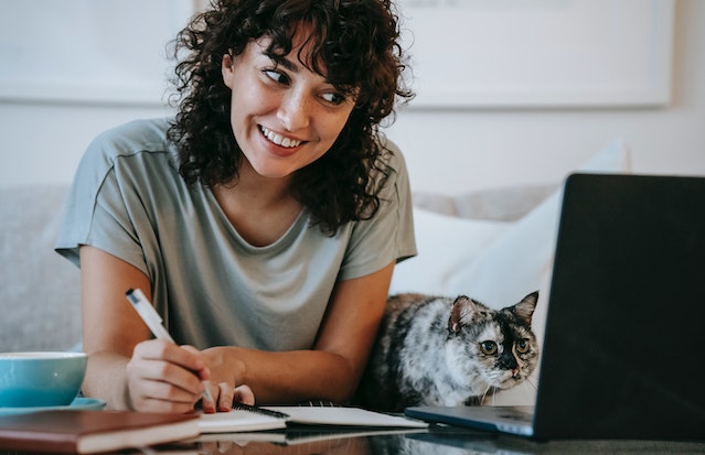 woman writing down in notebook facing computer